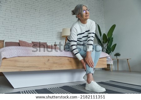 Senior woman suffering from leg pain while sitting on the bed at home