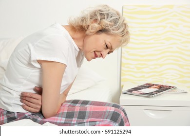Senior woman suffering from stomachache while sitting on bed at home