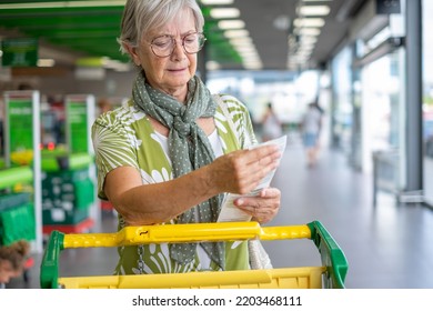 Senior woman in the supermarket checks her grocery receipt looking worried about rising costs - consumerism concept, rising prices, inflation - Powered by Shutterstock