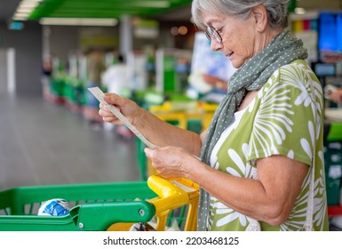 Senior woman in the supermarket checks her grocery receipt looking worried about rising costs - consumerism concept, rising prices, inflation - Powered by Shutterstock