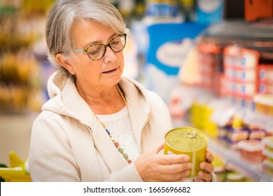 Senior Woman At The Supermarket Reading The Label Carefully On A Tin Jar. Active Elderly People Everyday Life Concept