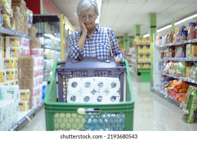 Senior Woman In Supermarket Worried For The Rising Costs Pushing Shopping Cart