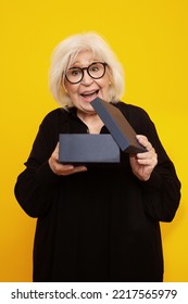 Senior Woman With Surpricwe Face Opening A Box On Yellow Background