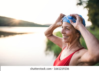 Senior Woman In Swimsuit Standing By Lake Outdoors Before Swimming.