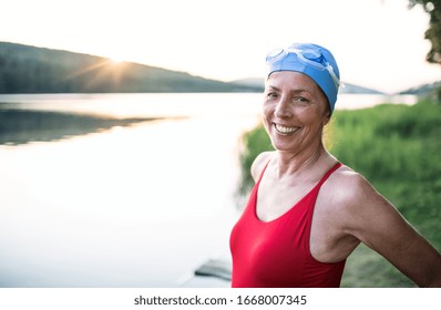 Senior Woman In Swimsuit Standing By Lake Outdoors Before Swimming.