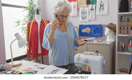 Senior woman tailor on phone in atelier with sewing machine, mannequin, and sketches - Powered by Shutterstock