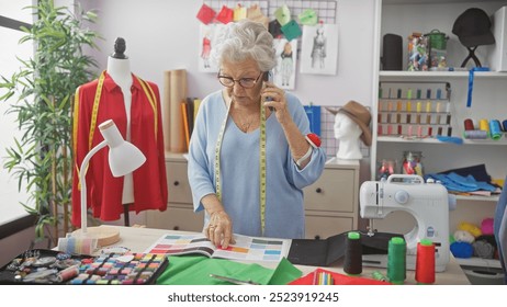 A senior woman tailor in a workshop, on the phone, surrounded by colorful fabrics and a sewing machine. - Powered by Shutterstock