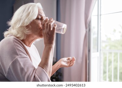 Senior woman takes pill with glass of water in hand.  - Powered by Shutterstock