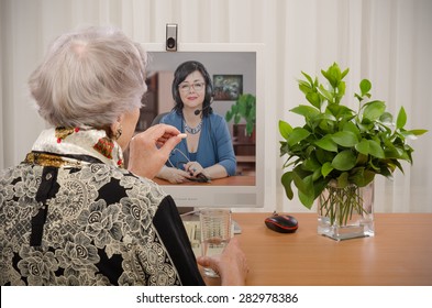 Senior Woman Taking A Pill In Front Of Virtual Doctor. Smiling Physician Is Consulting Her On The Monitor