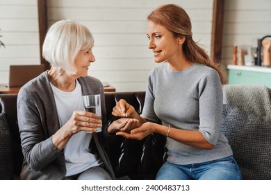 Senior woman taking pills from her daughter while holding glass with water. Side effect of drugs, memory loss, medications from dementia and mental issues - Powered by Shutterstock