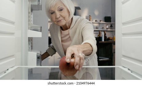 Senior Woman Taking Ripe Red Apple From Fridge In Kitchen