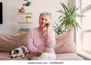 Senior Woman Talking On Her Mobile Phone. Mature Woman Has A Happy Conversation At Cellphone. Smiling Elderly Woman Using Phone Sitting On Couch At Home.