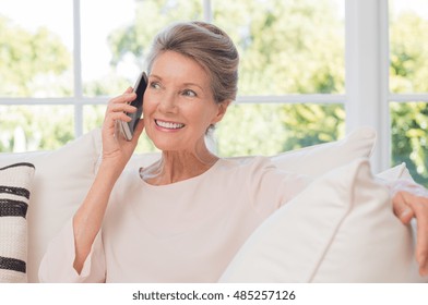 Senior Woman Talking On Her Mobile Phone. Senior Woman Has A Happy Conversation At Cellphone. Smiling Senior Woman Using Phone Sitting On Couch At Home.