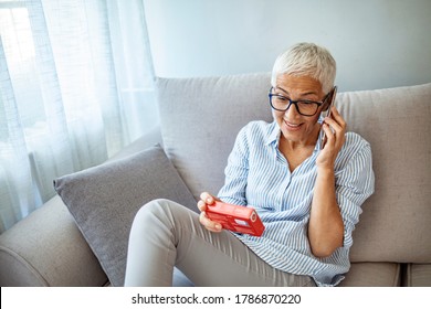 Senior woman talking on the phone and holding a pack of pills.  Woman refilling her medication prescription drugs online using smart phone technology app in her home