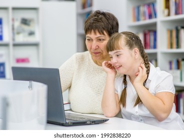 Senior woman teaches a young girl with down syndrome to use a laptop. Education for disabled children concept