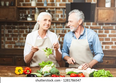 senior woman tossing salad and looking at the camera with man slicing vegetables