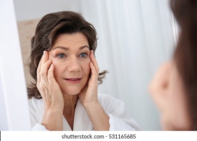 Senior Woman Touching Face In Front Of Mirror, Closeup