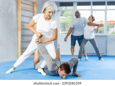 Senior woman train in pair with middle-aged coach to strike and reflect blows of enemy. Intense moment as two individuals engage in self-defense training, showcasing skill, reaction, repulse - Powered by Shutterstock