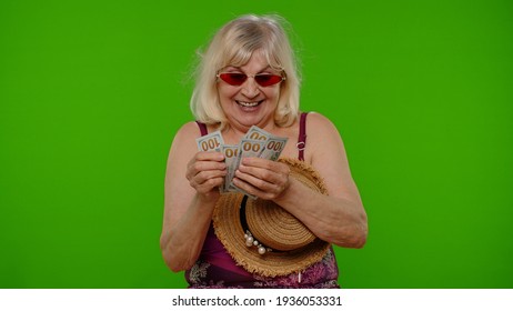 Senior woman traveler tourist counting bunch of dollars cash. Income, saving, credit for vacation. Elderly grandmother in swimsuit ready for summer holiday sea trip. Chroma key