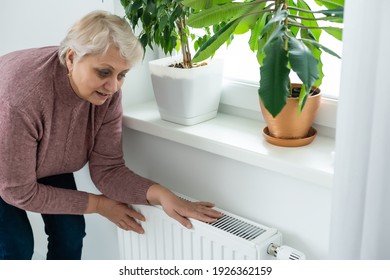 Senior woman trying to keep warm by warming hands on the heating radiator in winter time