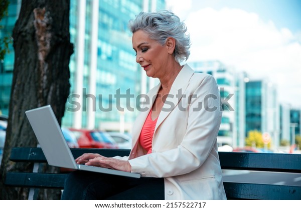 Senior\
Woman typing on laptop computer, sitting in open car showroom.\
Elderly Professional car dealer working at auto showroom.\
Saleswoman at automobile dealership, copy\
space