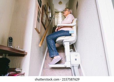 Senior woman using automatic stair lift on a staircase at her home. Medical Stairlift for disabled people and elderly people in the home. Selective focus