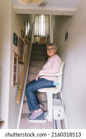 Senior woman using automatic stair lift on a staircase at her home. Medical Stairlift for disabled people and elderly people in the home. Vertical card. Selective focus.