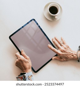 Senior woman using a digital tablet top view on working table with coffee in the office, business woman holding tablet in hands - Powered by Shutterstock