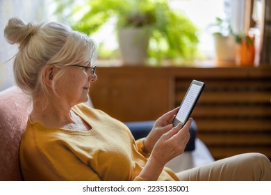 Senior woman using e-reader and reading an e-book at home
				