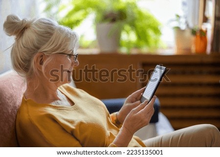Senior woman using e-reader and reading an e-book at home
