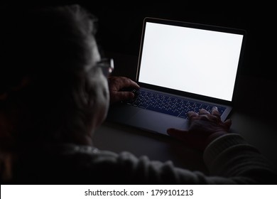 Senior Woman Using Laptop In Dark Room. Elderly Woman's Hands On A Computer Keyboard In The Dark, Light From The Screen. The Older Generation Is Searching For Information And Working 