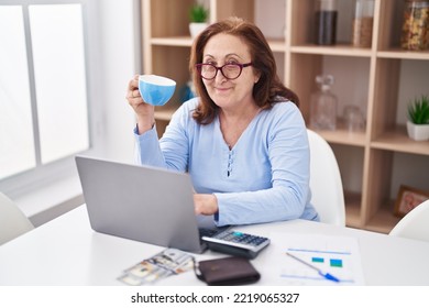 Senior Woman Using Laptop Drinking Coffee At Home