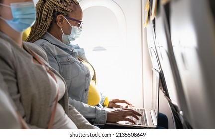 Senior woman using laptop during airplane trip while wearing face mask - Powered by Shutterstock