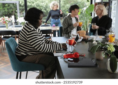 Senior woman using laptop at home, people in background - Powered by Shutterstock