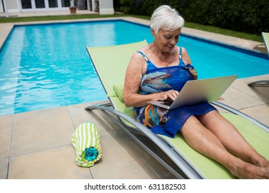 Senior woman using laptop on lounge chair at poolside - Powered by Shutterstock