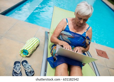 Senior woman using laptop on lounge chair at poolside - Powered by Shutterstock