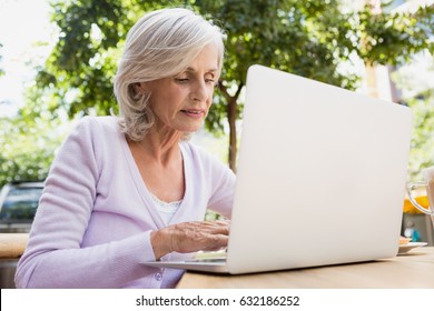 Senior woman using laptop in outdoor cafÃ© on a sunny day - Powered by Shutterstock