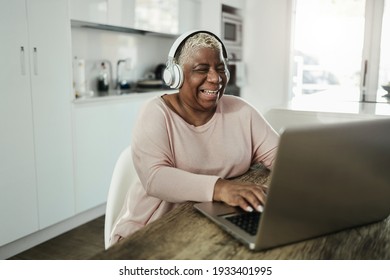 Seniorin, die ihren Laptop bei sich zu Hause mit Kopfhörern trägt - Joyful Senior Lifestyle and Technology Concept - Fokus auf Gesicht