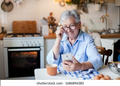 Senior Woman Using Mobile Phone At Home Kitchen. Happy Retired Person Shopping Online. People Connection, Virtual Communication, Distance Healthcare. Pensioner In Social Distancing, Isolation.