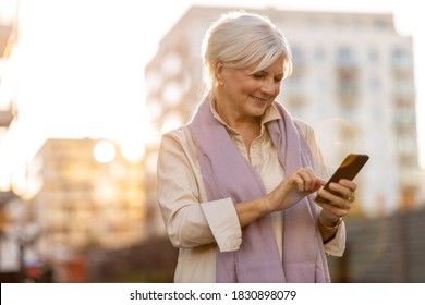 Senior Woman Using Mobile Phone Outdoors At Sunset
