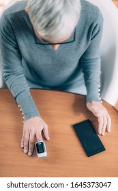 Senior Woman Using Pulse Oximeter And Smart Phone, Measuring Oxygen Saturation