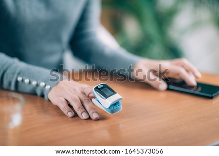 Senior Woman Using Pulse Oximeter and Smart Phone, Measuring Oxygen Saturation