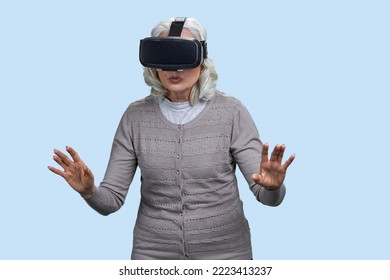 Senior Woman With Virtual Reality Headset Is Shocked By VR Experience. Isolated On Blue.