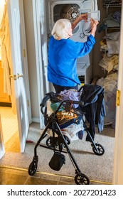 A Senior Woman With A Walker Does Laundry At Home.