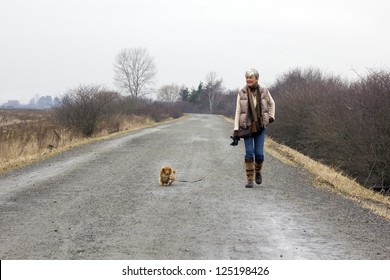 Senior Woman Walking Her Dog On An Overcast Winter Day.