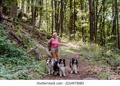 Senior Woman Walking With Her Three Dogs In Forest.