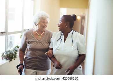 Senior woman walking in the nursing home supported by a caregiver. Nurse assisting senior woman.