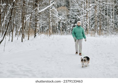 Senior woman walking in winter forest with her small dog - Powered by Shutterstock