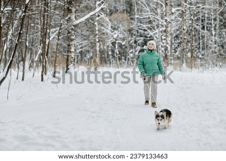 Senior woman walking in winter forest with her small dog