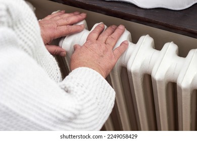 Senior woman warming hands on the heating radiator - Shutterstock ID 2249058429